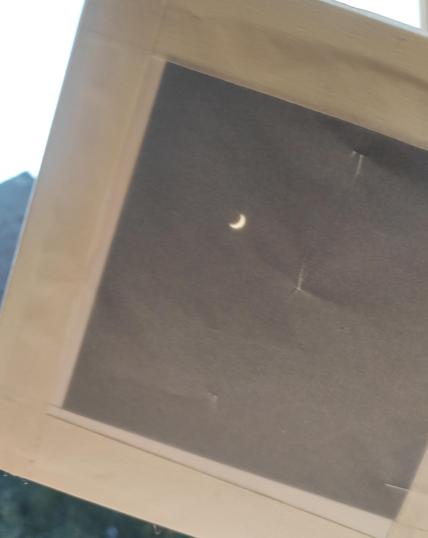 Picture of a partial eclipse with a thin sicle of the sun visible prejected on waxpaper through a pinhole camera