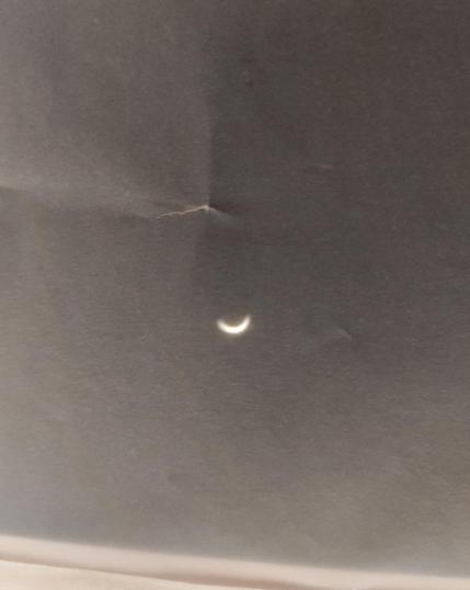 Picture of a partial eclipse with a thin sicle of the sun visible prejected on waxpaper through a pinhole camera