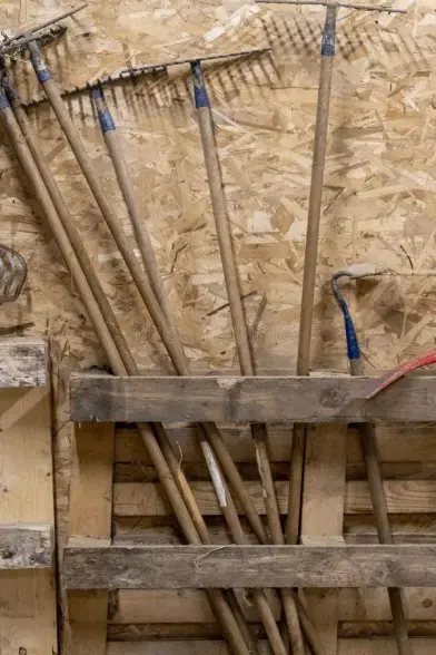 Eine alte Europalette an einer Holzwand. Darin stecken mehrere Rechen (eigentlich ja Harken).
