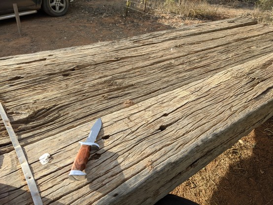 A knife laid out on a wooden table constructed from railway sleepers. The aesthetic is reminiscent of a scene in Terminator 2 where Sarah Connor carves
