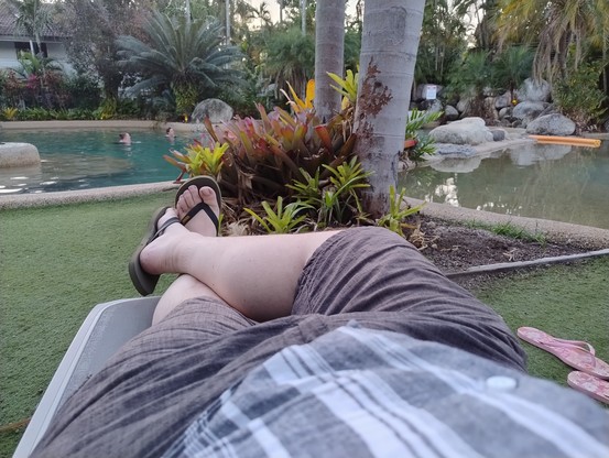 Pov photo of my feet stretched out on a lounge chair by a pool in the dim evening light