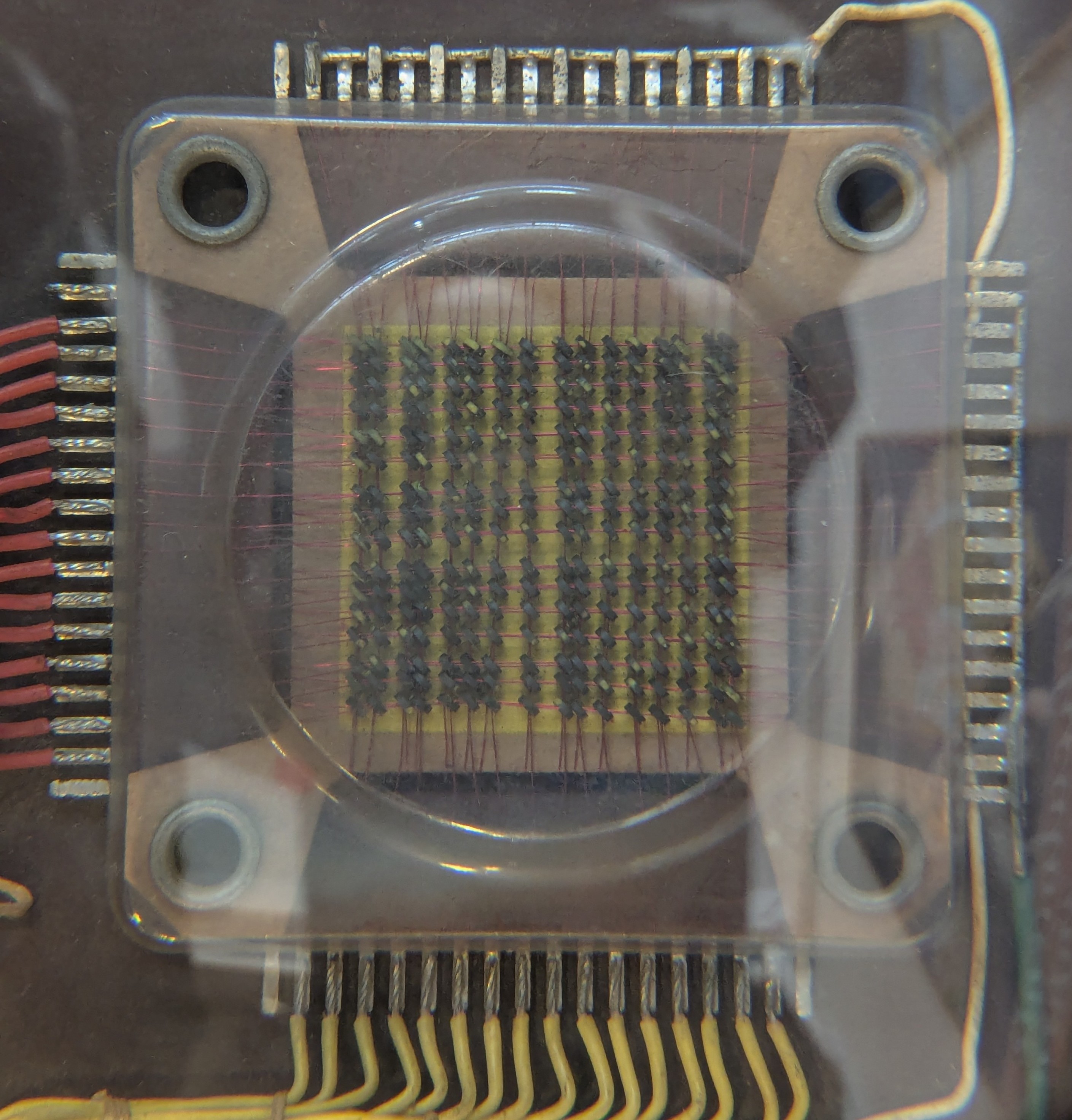 Memory core organized in an 8x32 grid of magnetic toroids. On the side, terminals connecting the wires that go through the toroids can be seen. The toroids are under a transparent covering Memory core organized in an 8x32 grid of magnetic toroids. On the side, terminals connecting the wires that go through the toroids can be seen. The toroids are under a transparent covering