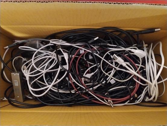 View looking down on the contents of a cardboard box which is a tangled mess of dozens of USB cables, and one not-USB cable.  Kids, can you spot the impostor?