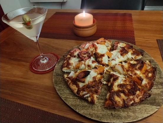 A table with a candle on it, and also a pizza on a board and a martini with three olives
