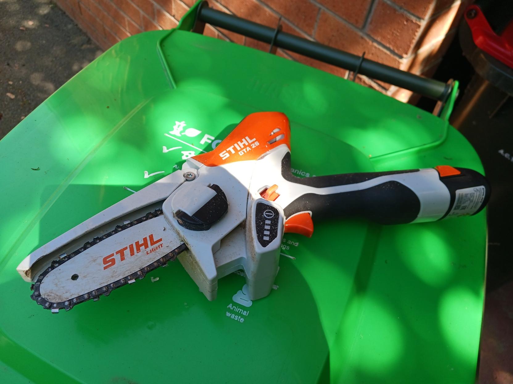 a small Stihl electric chainsaw sitting on a bright green wheely bin lid