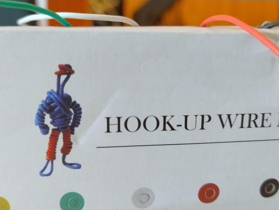 Side of a box labelled Hook Up Wire featuring a picture of a little guy made of wire strands and inclining a jaunty red hat