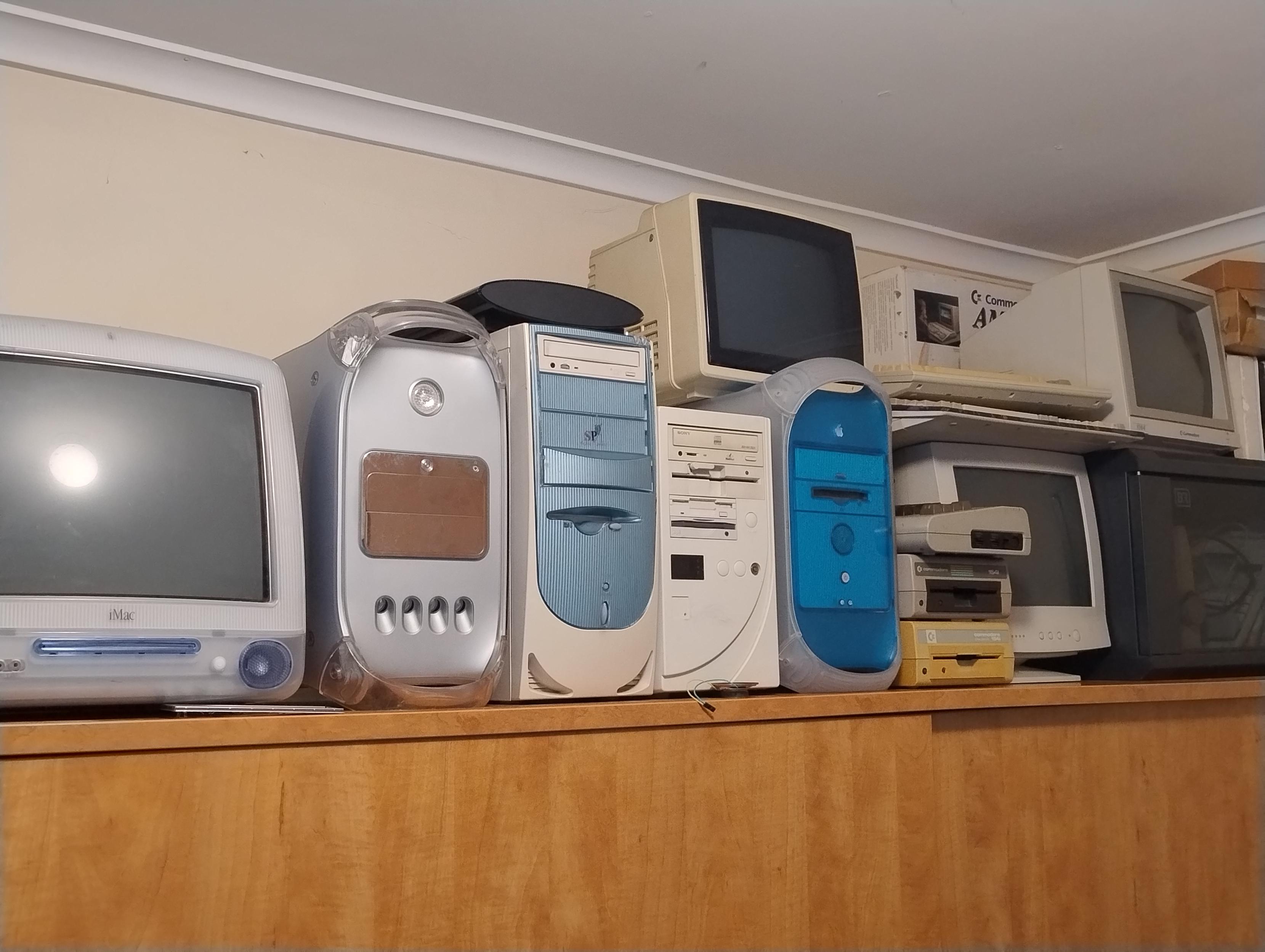 The top of a wardrobe on which is placed a CRT iMac, a mirror door G4 Mac, two PC tower cases, a blue and white G3 Mac, two commodore 1541 disk drives, a couple of Commodore 64s, an Amiga 500 and a few CRT monitors
