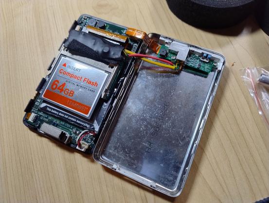 An older iPod, case opened, showing a 64GB CF card inside and a black plstic-coated blob with some wires running from it to the headphone jack area.