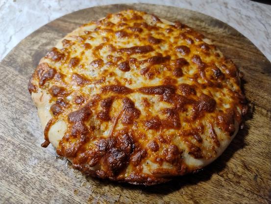 A delicious looking garlic pizza on a wooden board, as yet unsliced.