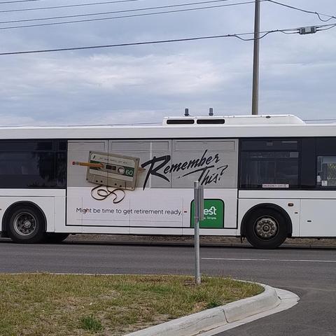 A bus with a big advertisement on the side featuring an audio cassette with a pencil being used to spool some loose tape back inside it, and the text 