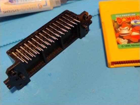 A black cartridge socket for a game boy with its many tiny pins showing, on a blue mat next to a Donkey Kong cartridge 