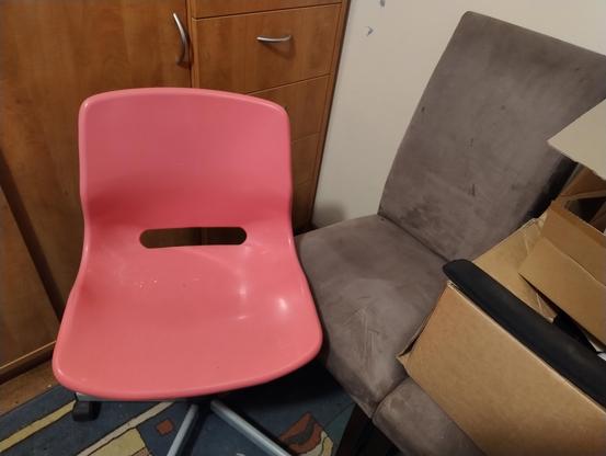 A pink IKEA office chair next to a velvety textured dining chair, which is beside an identical twin of itself that's obscured by boxes.
