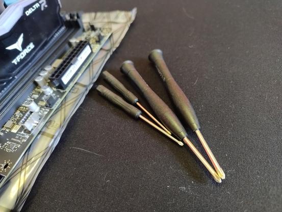 Four tiny, shitty, cheap Philips screwdrivers on a table next to the edge of a motherboard