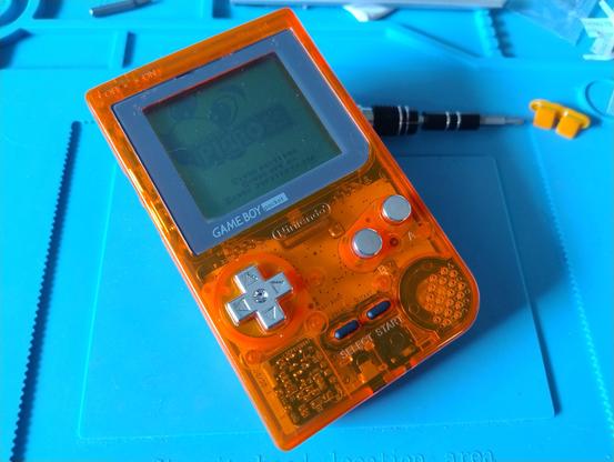 A Game Boy Pocket in a transparent orange shell with chrome buttons, displaying the Picross start screen
