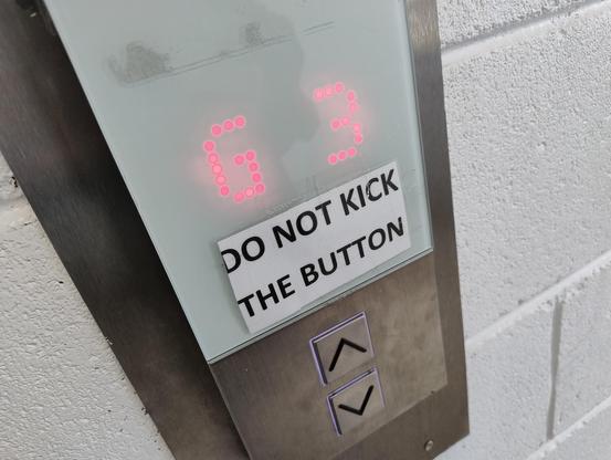 An elevator lobby area with up and down call buttons, and a later-added sign saying