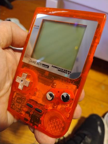 A Game Boy Pocket with a transparent orange shell, and shiny chrome buttons and screen frame