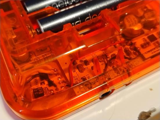Close up view of a transparent orange shell on a Game Boy Pocket showing extra wires running across the circuit board inside