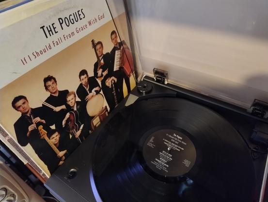 A turntable with a copy of If I Should Fall From Grace With God, by The Pogues on it, with the album cover next to it.