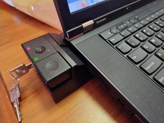 Corner of a ThinkPad attached to a dock, which has a key sticking out the side of it and a red icon of a lock lit up