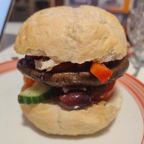 A bread roll sliced in half with bits of capsicum, cucumber, olives and feta poking out the edges and a big fat mushroom in the middle