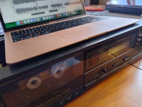 A pink MacBook on top of a Technics tape deck with the lid off, and a cassette in it