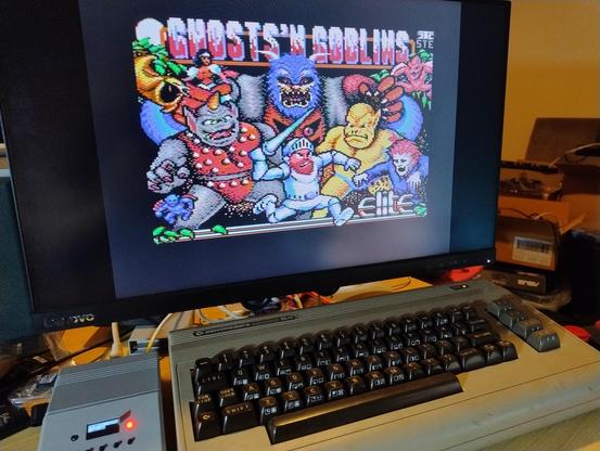 Intro screen for ghosts and goblins on a monitor, with a Commodore 64 below it and a small grey box beside