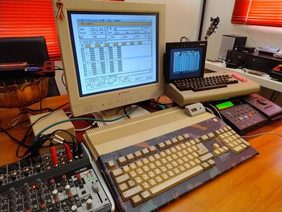 An Amiga, a Commodore 64, a Roland MT 300 and a small mixer on a table with octamed running on the Amiga and a small LCD display showing Cynthcart UI from the C64