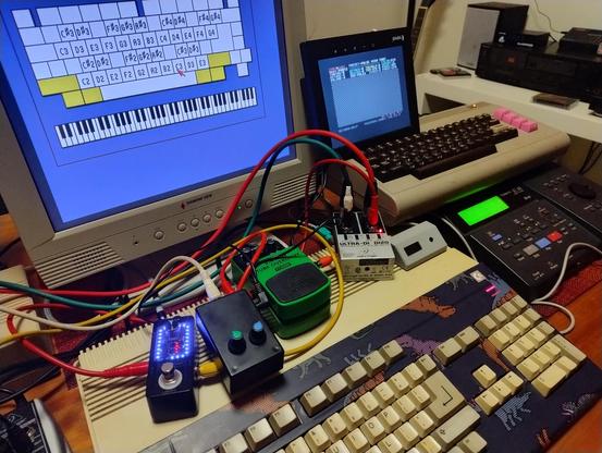 An Amiga 500, a Commodore 64, and a variety of cables and boxes including a couple of guitar pedals on a table