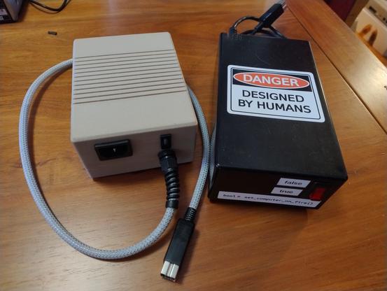 Two power supply bricks on a table, one in beige with ventilation gaps, the other plain black with a front red switch and prominent