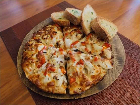 Pizza cut into six slices on a board with four slices of toasted sourdough bread on the side