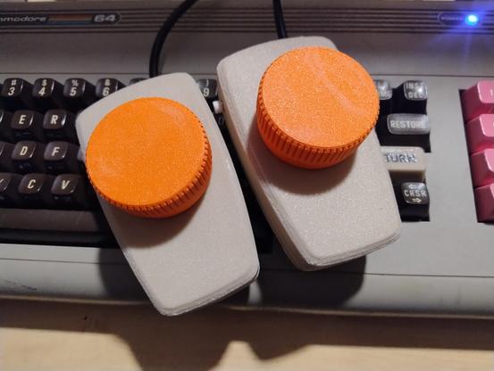 A pair of paddle controllers with bright orange knobs on top of a Commodore 64
