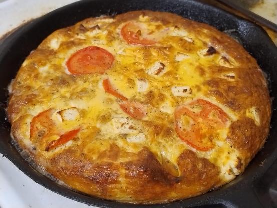 Baked frittata in a skillet, with sliced tomatoes and chunks of feta visible on top