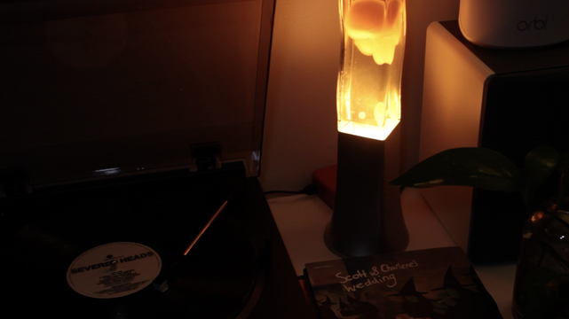 A lava lamp with a big chunk of wax about half way down, on a table with a turntable loaded up withc a copy of Since the Accident by Severed Heads playing on it.