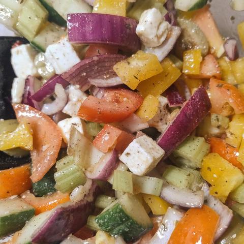 Chopped red onion, tomato, cucumber, yellow capsicum, celery, olives, and feta in a bowl