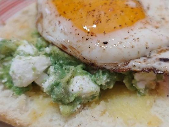 A fried egg atop avocado and feta atop toast