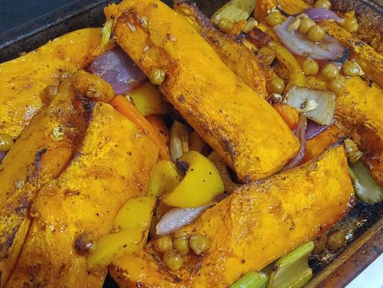 Big slices of roasted pumpkin on a baking dish alongside carrots, chickpeas, celery, capsicum and onion 