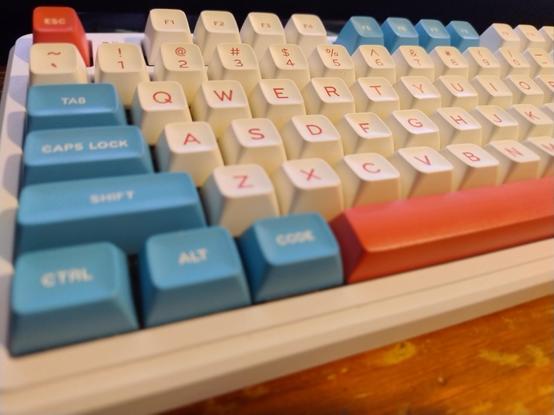Close up of a keyboard with rounded retro styled keys with bold text only labels, in pale red and blue function keys and white letters and numbers