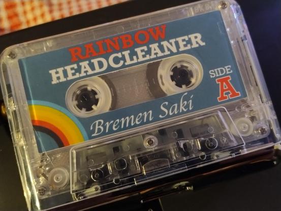 An audio cassette in a player, the label shows it's Rainbow Headcleaner by Bremen Saki 