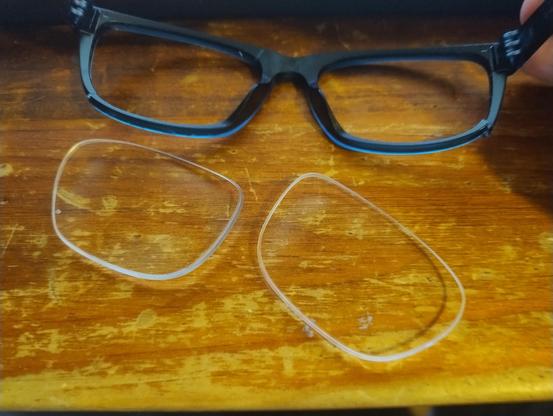 Blue glasses frame with cracks under the lens area and two lenses on the table next to it