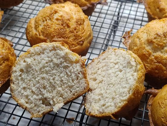 A muffin cut in half on a cooling rack adjacent to many uncut muffins 