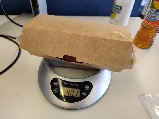 A cardboard box with just a cheeky glimpse of a bread roll visible inside it, on kitchen scales reading 401 grams