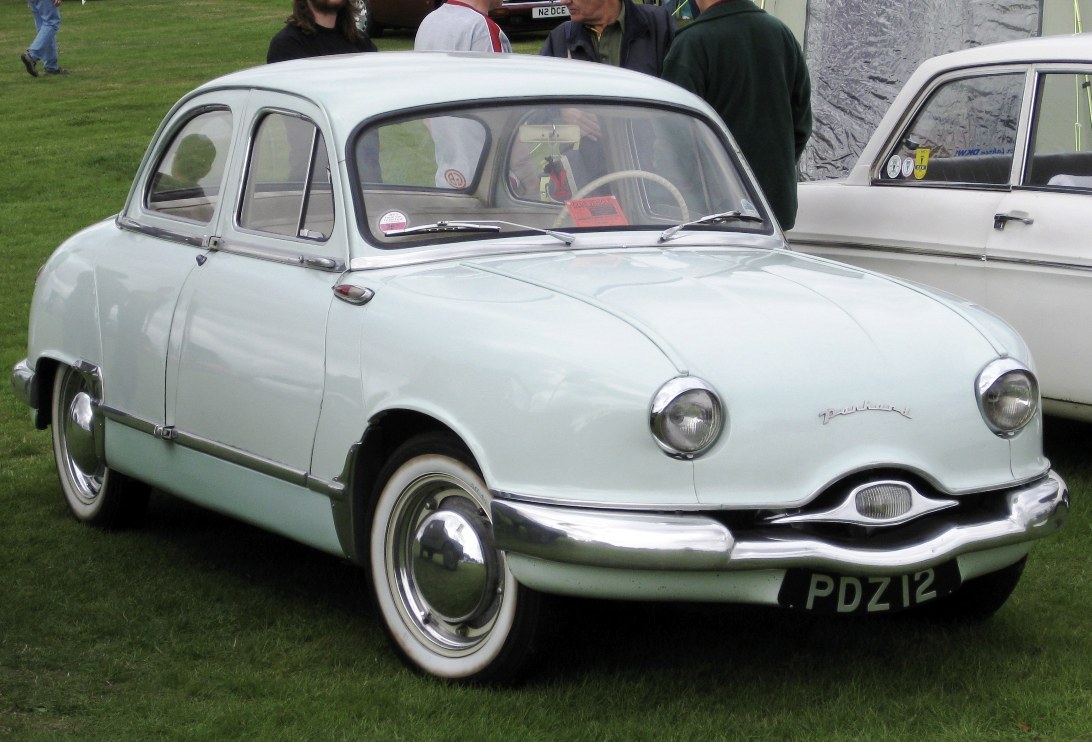 A little blue car with 2 doors, it is very round and has little circle headlights and a very small grille, it almost looks like it has a face.