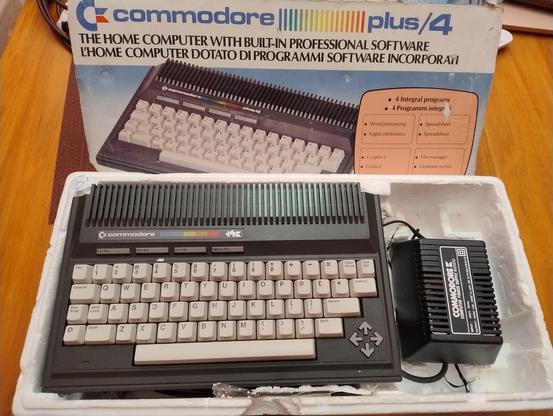 A Commodore Plus 4 computer in it's retail box with power supply next to it..