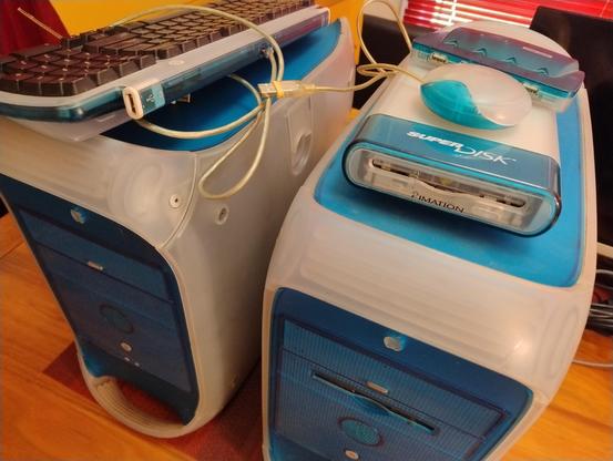 Two Blue and White G3 cases side by side with matching peripherals on top. keyboard, mouse, USB hub, and imation USB Super Disk floppy drive 