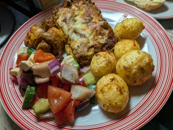 Lasagna on a plate with Greek salad, roasted potatoes, and mushrooms. 