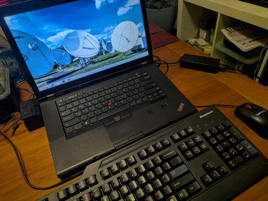 A ThinkPad T530 at a gnome desktop attached to a dock with a key lock on the side, and a Lenovo keyboard and mouse set in front 