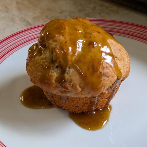 A muffin on a plate with a thick carmel coloured sauce drizzled over the top
