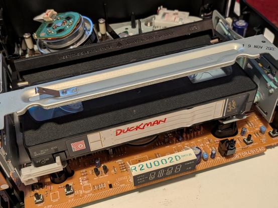 A vhs tape in a VCR with the cover removed exposing the internals and a hand written label 